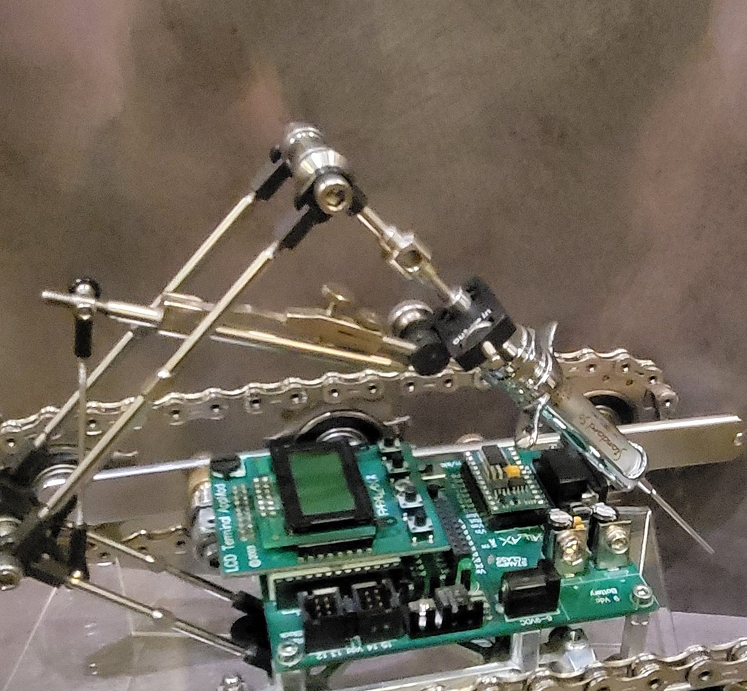 Figure 3 — The manipulator: a triangular truss of polished rods cantilevers off
the front of the chassis and presents the vintage glass syringe, needle forward,
at its apex. Sculpture courtesy of C…