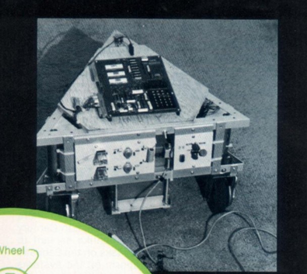 Figure 2 — Overhead view of the assembled Stage I chassis. The triangular
footprint of the angle-aluminum frame is visible, with the KIM-1 board on its
wooden mounting panel at the apex and an elec…